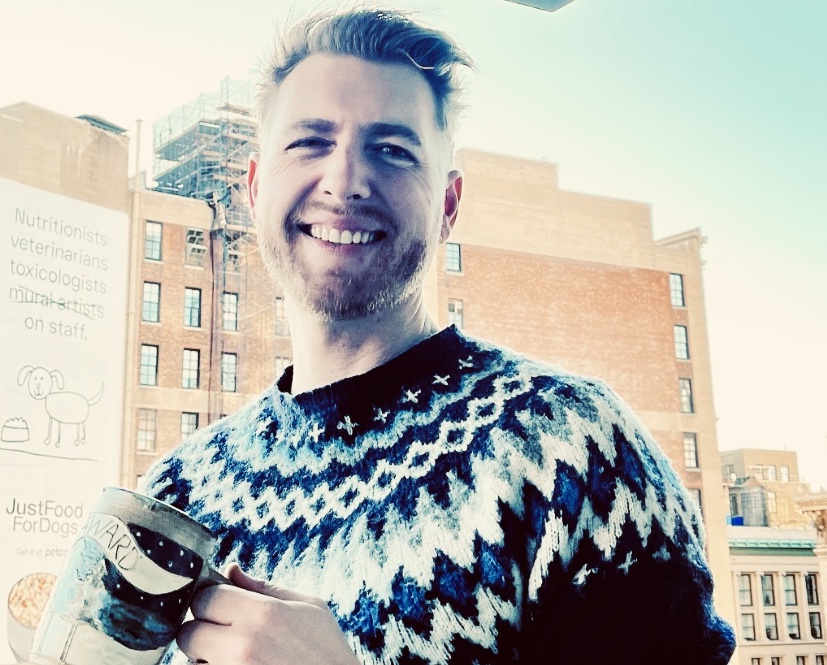 Front profile of Brandon Lewis with short hair wearing a multicolored sweater and a building in the background.