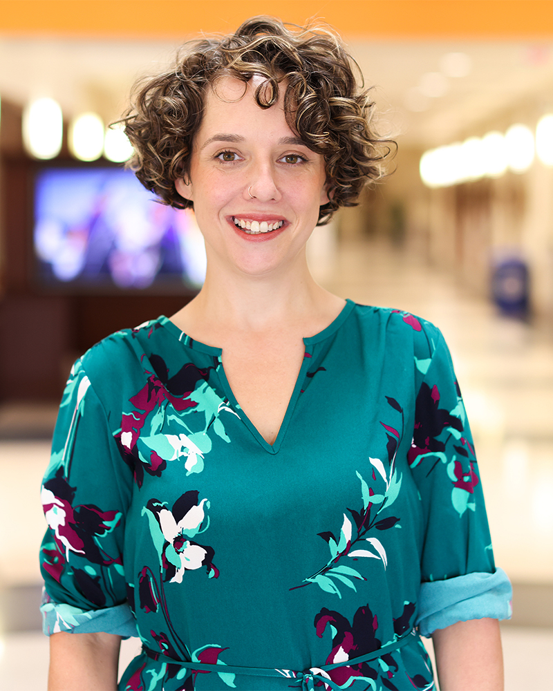 Eliza (Land) Blankenship Boles ('07), a young white woman with a curly mop in a green dress, stands in a library.