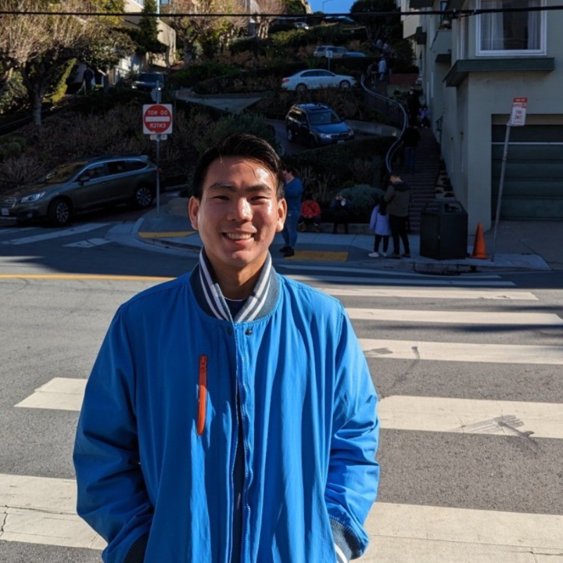 Ethan Lau ('22), young Malaysian man in a blue jacket, stands on a hilly city street.