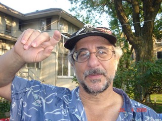 Front profile of Garry Cooper wearing glasses and a ball cap with graying hair and short trimmed beard in a blue collared shirt.