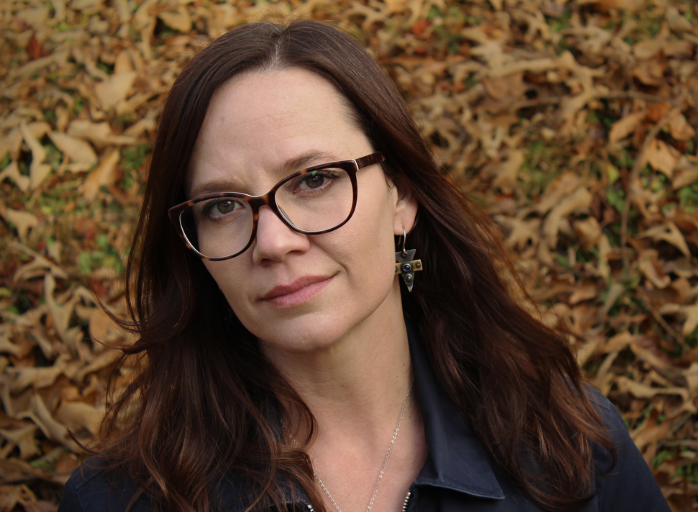 Rachel M. Hanson, brunette author in glasses against fall leaves.