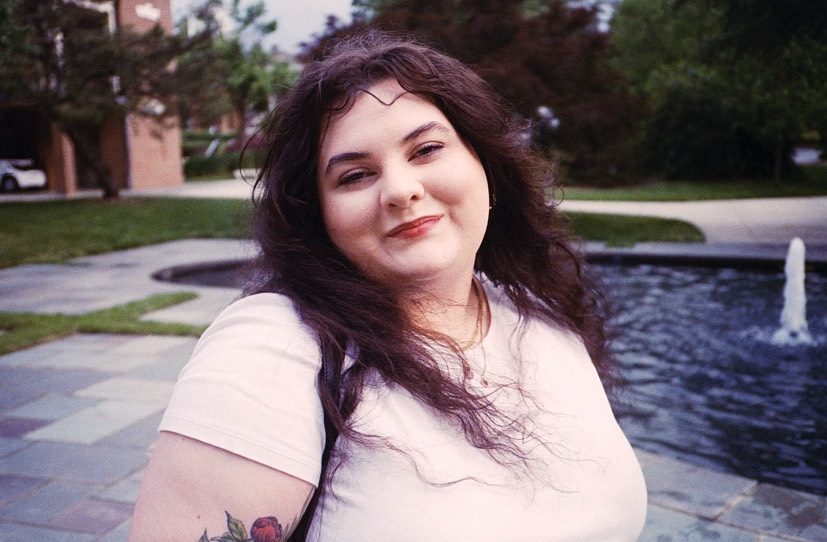 Lisa Compo headshot. Smiling brunette in front of water feature on a clear day.