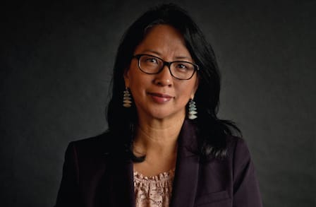 Front profile of Luisa A. Ingloria with black shoulder length hair wearing black rimmed glasses and a black suit jacket with a black background.