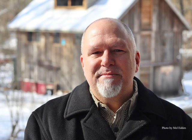 Author headshot of Matt Hohner by Mel Edden. Man with gray beard in pea coat in snowy outdoor landscape.