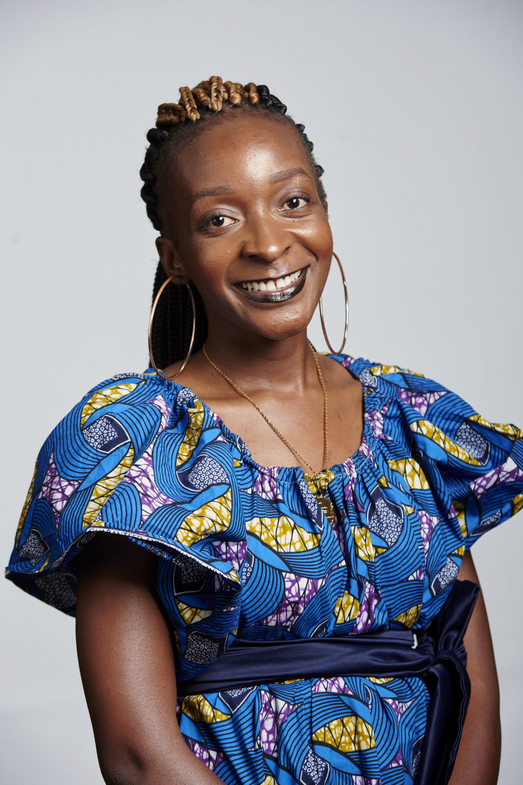 Portrait of Mubanga  Kalimamukwento with long black braided hair wearing a blue Zambian traditional dress and a blue background.