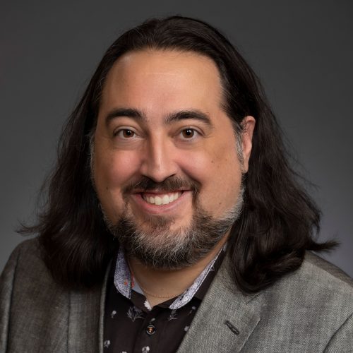 Portrait of Glenn Shaheen with long dark hair wearing a gray sport jacket.